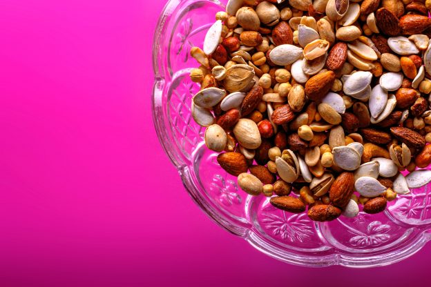 A glass bowl of assorted nuts against a pink backdrop